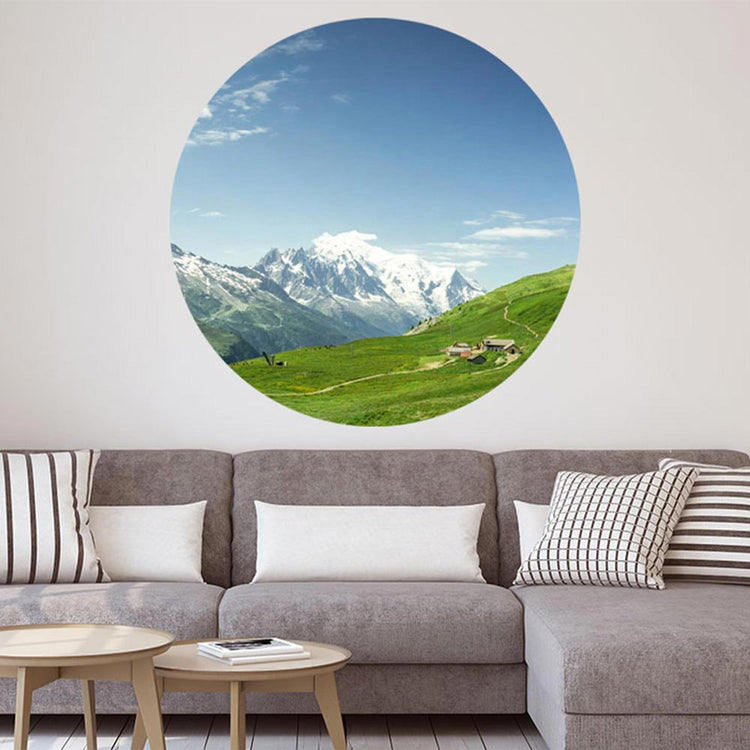 Ein großer, runder, Wandaufkleber mit einem Alpen-Wiesen-Motiv ist an einer Wand verklebt. Es ist eine Dekoidee über einer Wohn-Couch und für verschieden Räume möglich, die einen 3D Effekt schaffen.