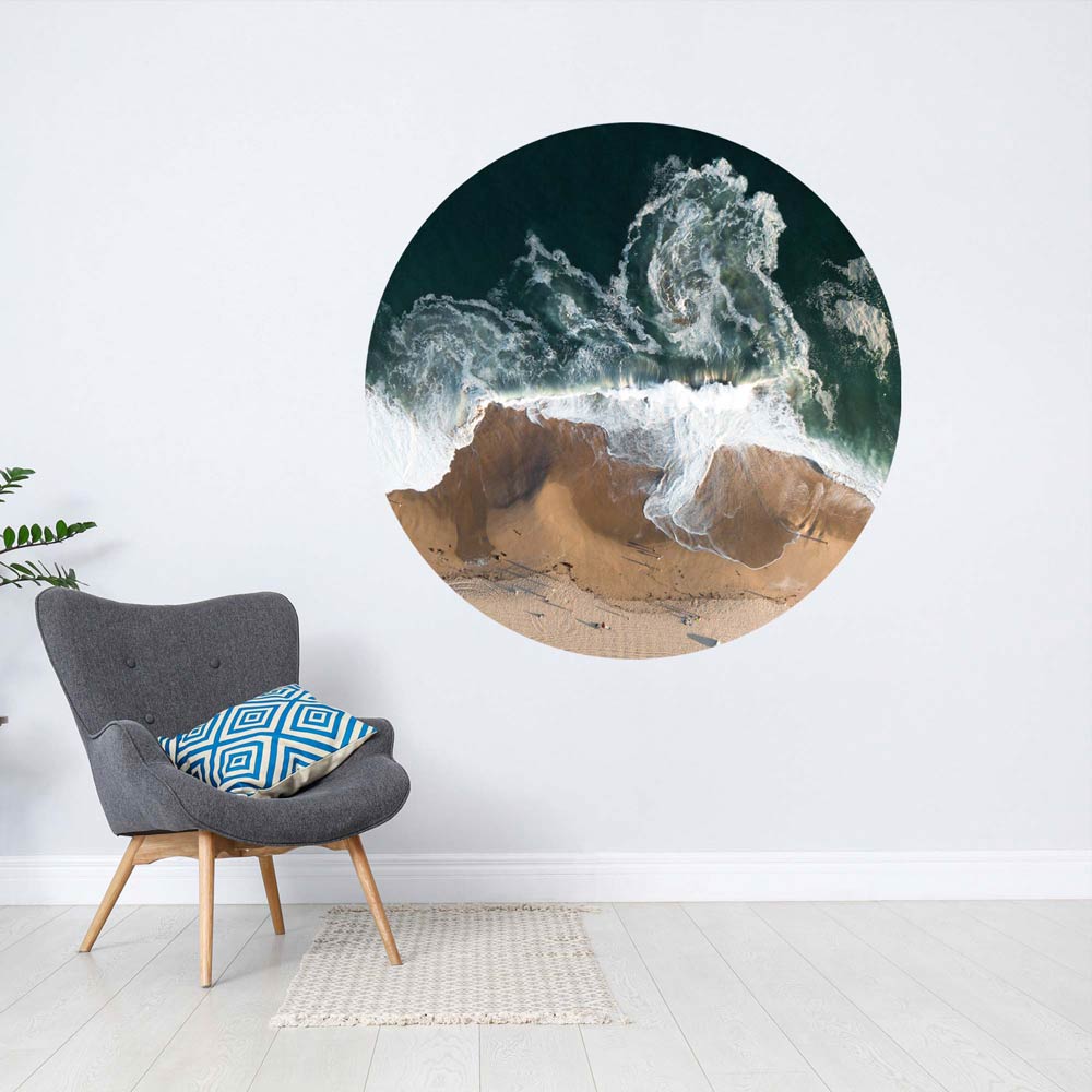 Vogelperspektive eines Strandes mit Wellen, die den Sand erreichen. Das Bild ist in einem Raum an der Wand zu sehen.