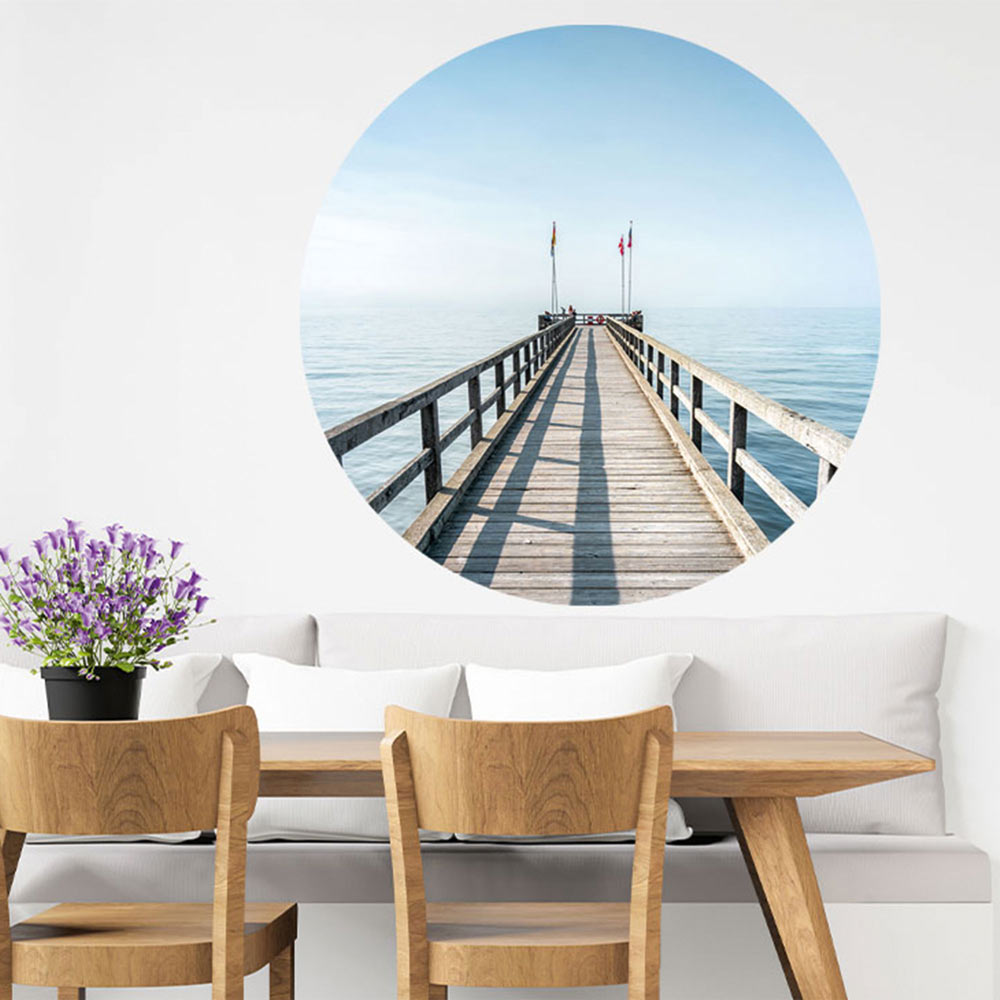 Großansicht eines runden Wandaufklebers mit einem Motiv vom Steg in der Nordsee. Das Bild schafft einen 3D Effekt und sorgt für eine Tiefe. Als Dekoidee ist es an einer weissen Wand verklebt über einer Essecke.