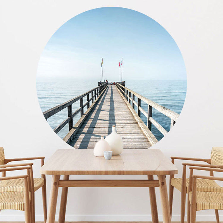 Großansicht eines runden Wandaufklebers mit einem Motiv vom Steg in der Nordsee. Das Bild schafft einen 3D Effekt und sorgt für eine Tiefe. Als Dekoidee ist es an einer weissen Wand verklebt über einem Esstisch aus Holz.