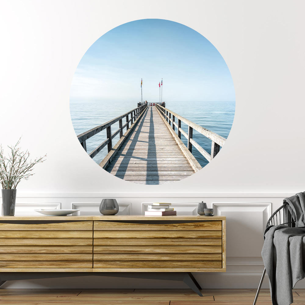 Großansicht eines runden Wandaufklebers mit einem Motiv vom Steg in der Nordsee. Das Bild schafft einen 3D Effekt und sorgt für eine Tiefe. Als Dekoidee ist es an einer weissen Wand verklebt über einer Kommode.