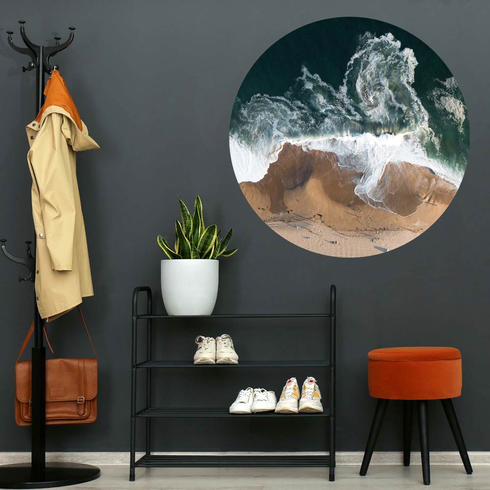 Vogelperspektive eines Strandes mit Wellen, die den Sand erreichen. Das Bild ist in einem Flur an der Wand zu sehen.