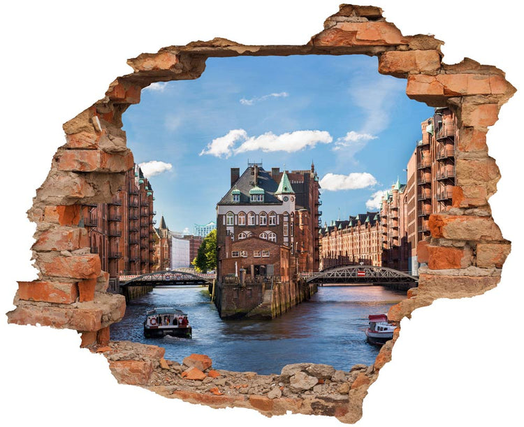 Wandtattoo mit 3D-Effekt einer aufgebrochenen Ziegelwand, die einen Blick auf die Speicherstadt in Hamburg freigibt, mit Brücken, Wasserwegen und historischem Gebäude im Zentrum.