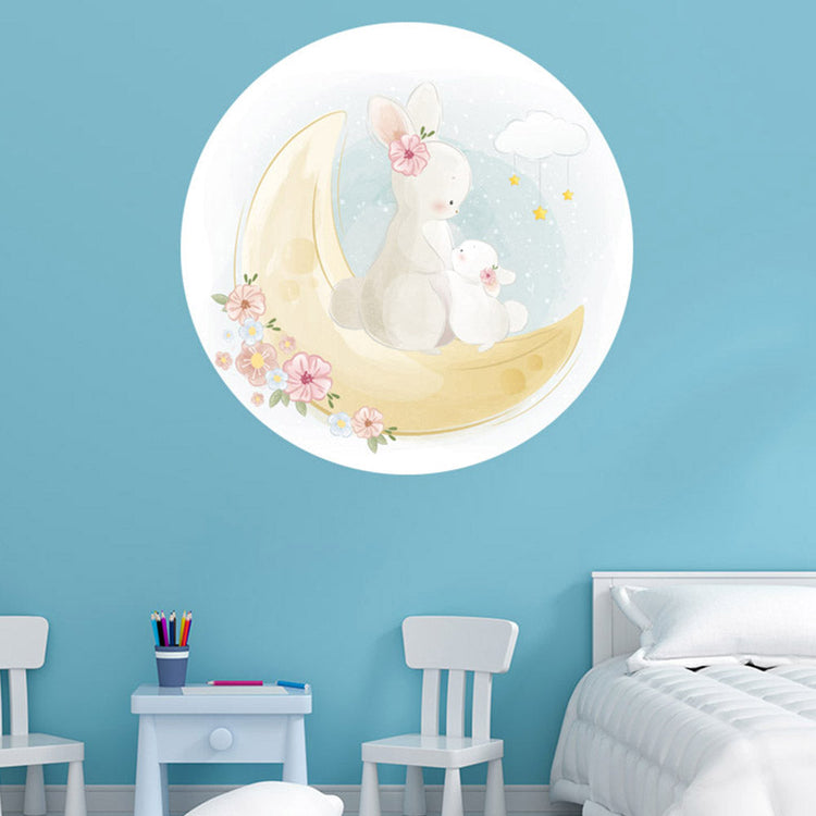 Wandtattoo rund "Mond und Hasen" auf blauer Wand im Kinderzimmer neben einem Bett.