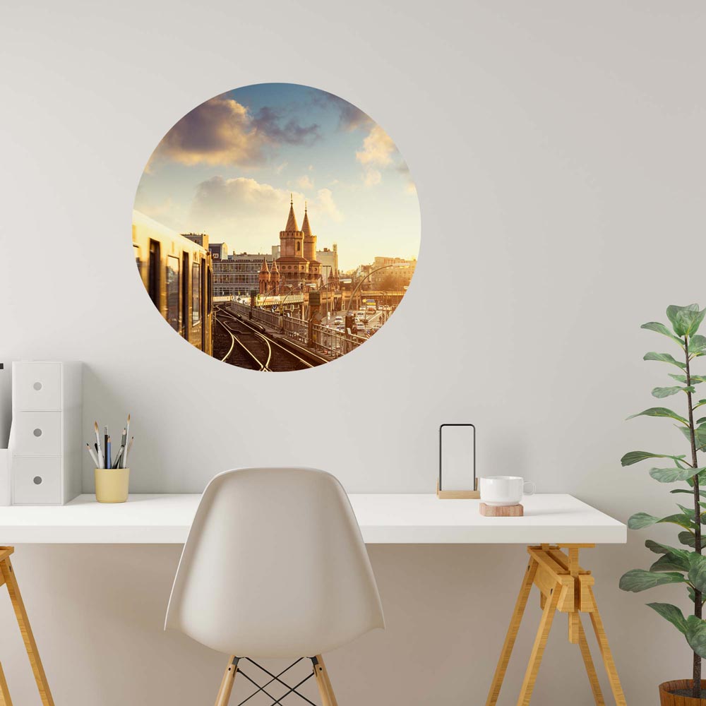 Modernes Büro mit rundem Wandtattoo der Berliner Oberbaumbrücke und einer vorbeifahrenden U-Bahn bei Sonnenuntergang.